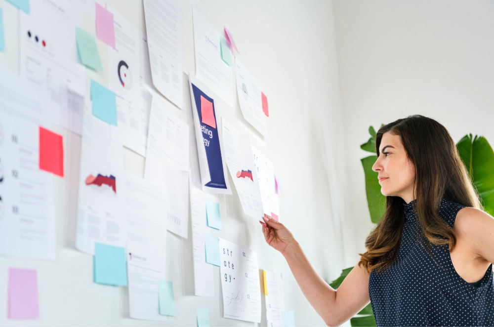 Woman looking at a white board of sticky notes and visuals