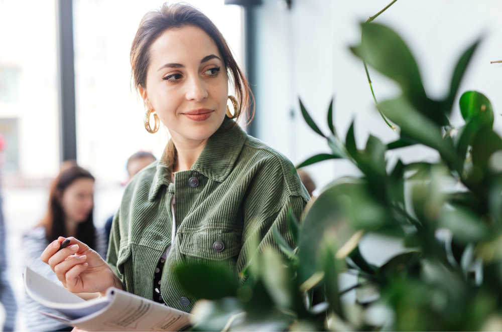 Woman taking notes by hand near an office plant